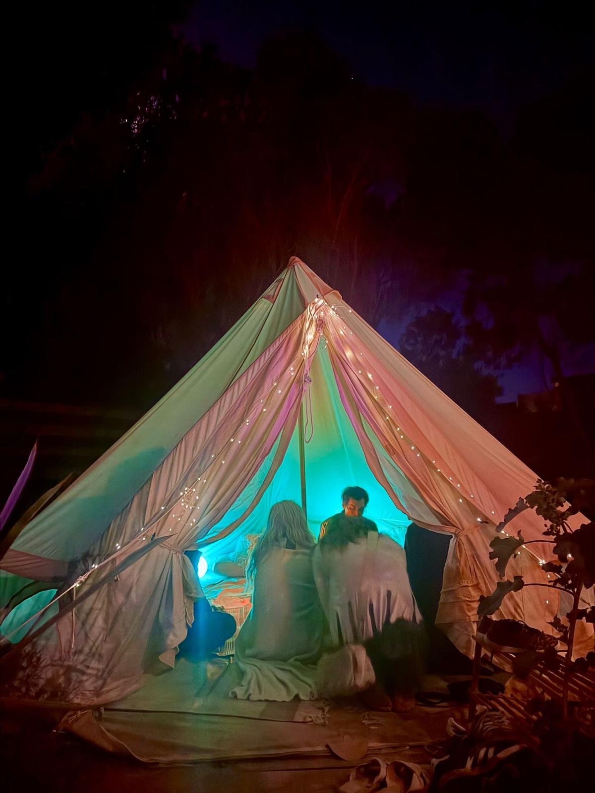 La Tarot Tent de Hotel Tarot: una carpa iluminada de noche, con personas sentadas adentro.