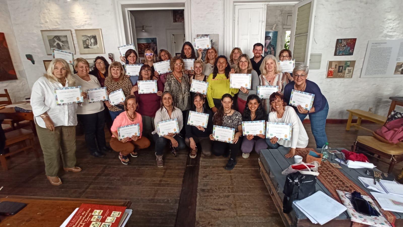 Un grupo de personas con sus diplomas en una casona con cuadros en las paredes.